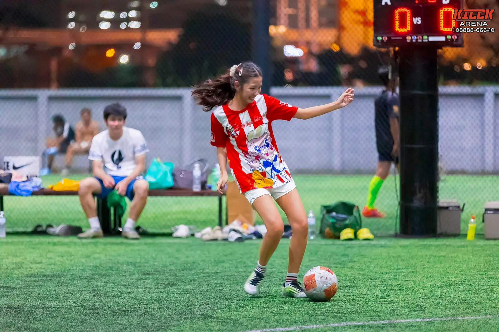 A player in a red-and-white shirt dribbles past the scoreboard
