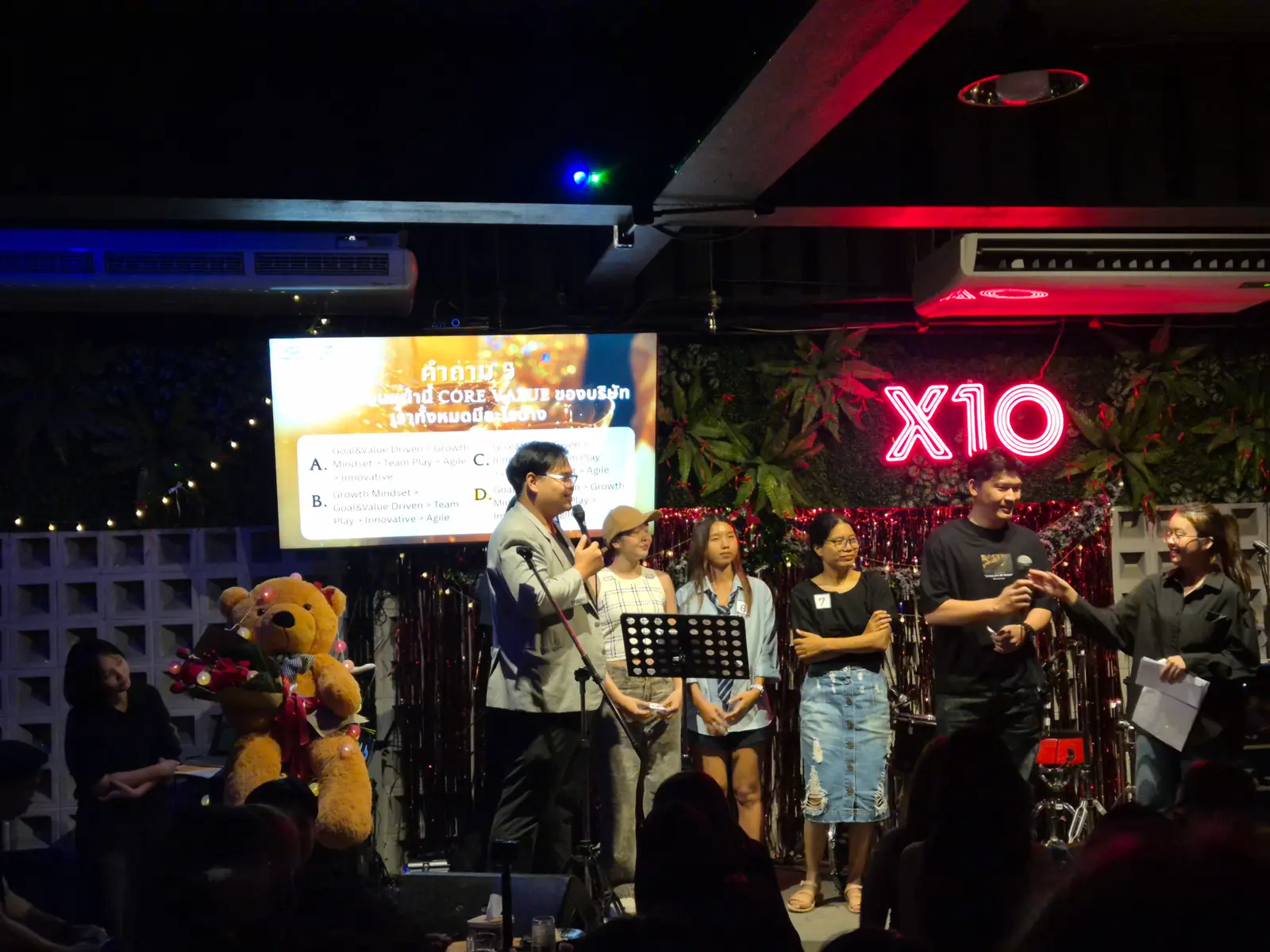 A multiple-choice quiz on screen, with the hosts and volunteers on stage